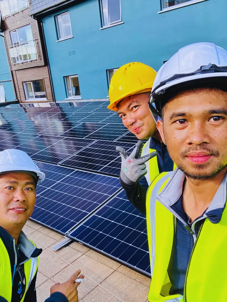 Three workers wearing hard hats beside solar panels